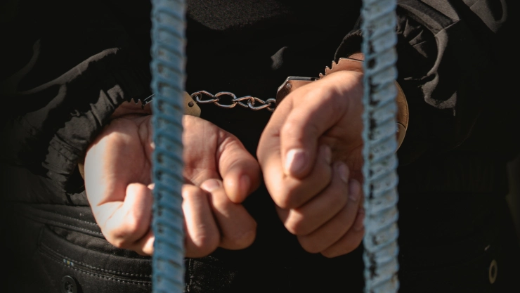 Unas manos esposadas tras unas rejas.