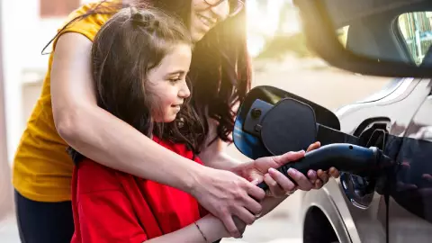 una mujer carga gasolina junto a su niña
