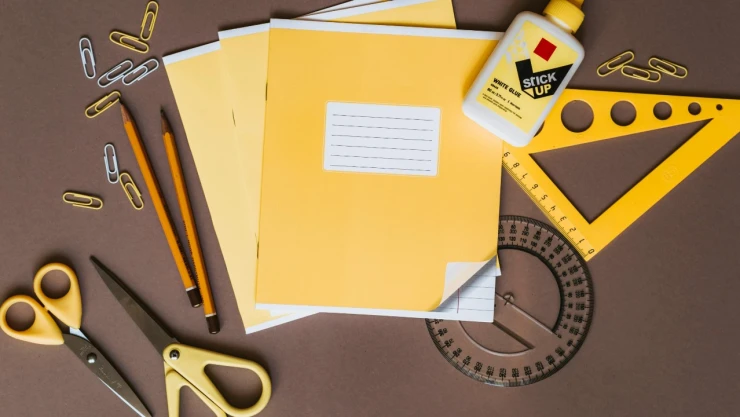 utiles_escolares_tijeas_clips_cuadernos_escuadras_pegamento_amarillos_fondo_cafe