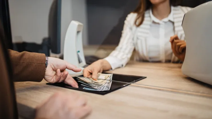 Una cajera de banco entrega dinero a una persona.