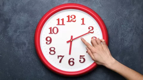 Una persona señala la hora en un reloj rojo de pared.