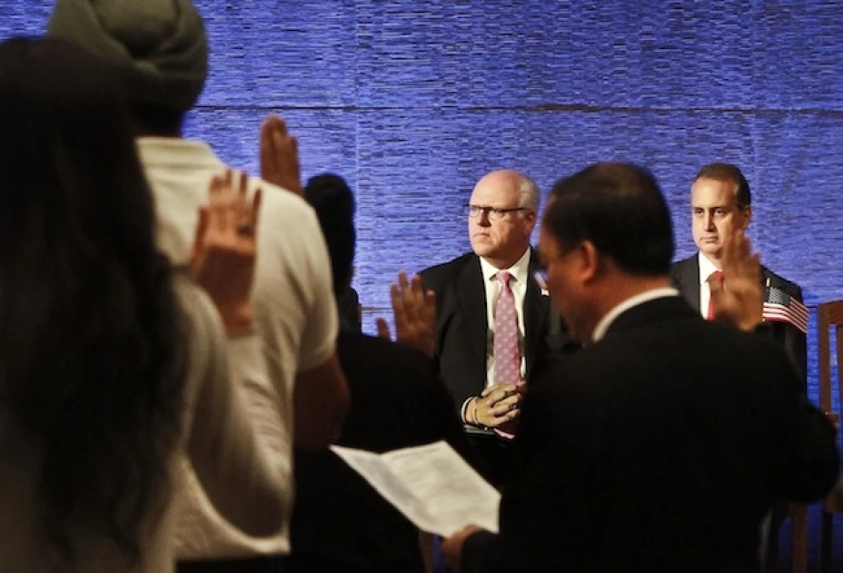 El representante federal Joseph Crowley (al fondo, centro), demócrata por Nueva York, y su colega Mario Diaz-Balart (al fondo, derecha), republicano por la Florida, observan mientras varios inmigrantes juramentan ante la bandera en una ceremonia de naturalización
