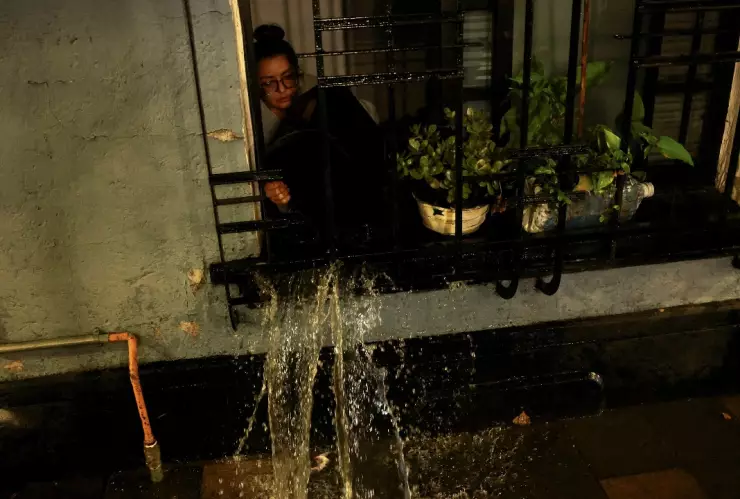 Una mujer retira el agua que inundó su departamento a través de una ventana que da a la calle, luego de fuertes lluvias en la Ciudad de México el 10 de agosto de 2025.