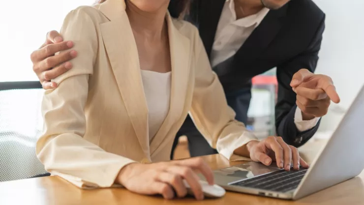 Un hombre toca a una mujer en su hombro mientras ella le enseña algo en una computadora.