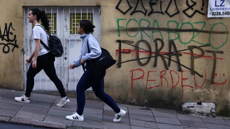Mujeres pasan junto a grafitis que dicen “Fuera Bozo”, “Fuera PT” y “Perdiste” un día después de que el senador brasileño de derecha Flavio Bolsonaro y el presidente de izquierda Luiz Inácio Lula da Silva avanzaran a una segunda vuelta tras la primera ronda de votación, en Porto Alegre, Brasil , 5 de octubre de 2026.