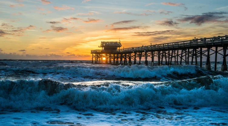 Las olas de la playa de Florida rompiendo en la costa y un largo muelle con el atardecer de fondo