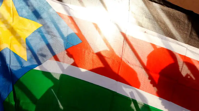 Siluetas de habitantes de Sudán del Sur vistas a través de una bandera de ese país.