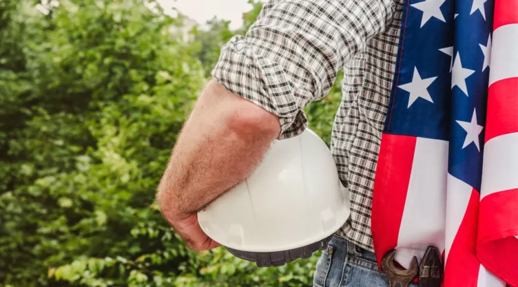 Un hombre sostiene un casco de obrero y una bandera de Estados Unidos.