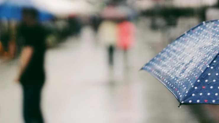 En primer plano, un paraguas azul en día lluvioso, con el fondo desenfocado. Ambiente urbano