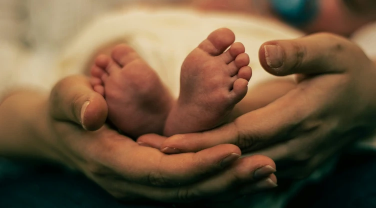 Pies de bebé sujetados por manos de adulto.