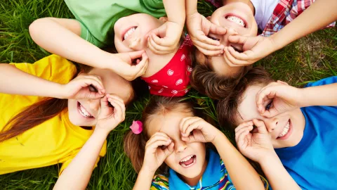 Niños acostados en el pasto poniendo sus manos en los ojos.