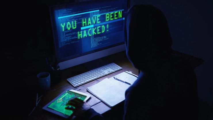 Un hacker realizando un trabajo de contraseñas, en la oscuridad, encapuchado y frente a la computadora