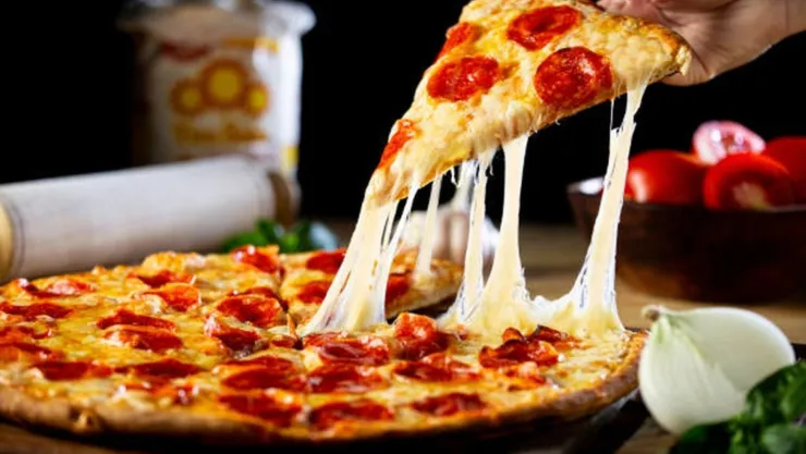 Una persona desprende un pedazo de una pizza que está encima de una mesa.