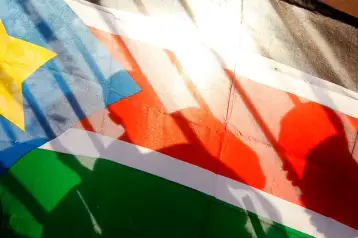 Siluetas de habitantes de Sudán del Sur vistas a través de una bandera de ese país.