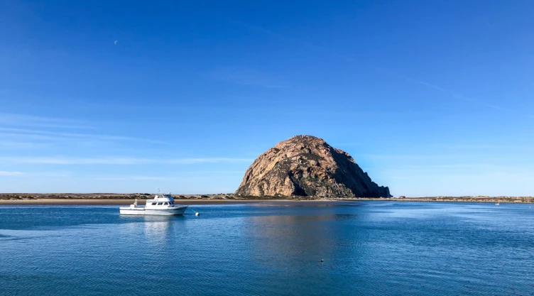 La Playa Morro Bay con una pequeña embarcación blanca navegando en el agua y el morro de fondo en el centro de la escena