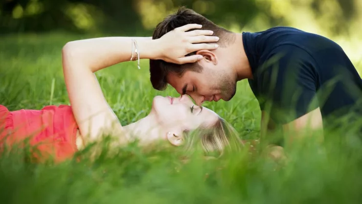 Pareja acostados en el pasto en un momento romántico, tocando frente a frente.
