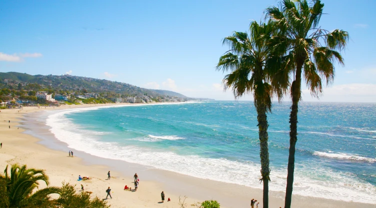 Playa de California con arena blanca, aguas turquesas y turistas caminando por la costa.