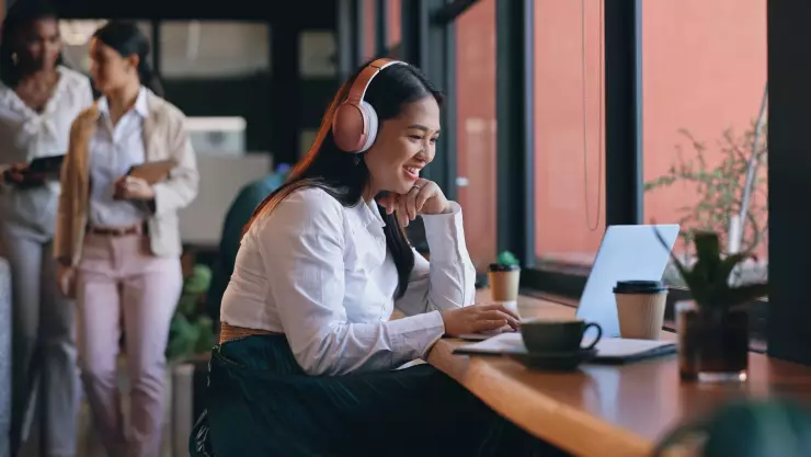 una mujer trabaja felizmente en una cafetería con su computadora a mano