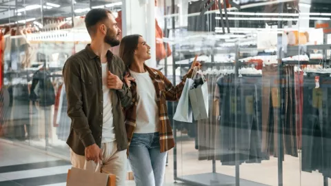 Una pareja camina en un centro comercial y mira un escaparate de una tienda de ropa.