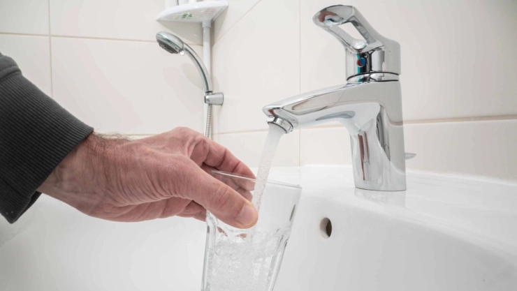 Un hombre se sirve agua del grifo en un vaso.