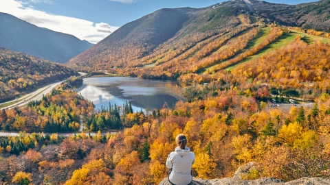 Una mujer sentada en una piedra, apreciando la inmensidad del parque estatal con las montañas, su vegetación y el río en escena