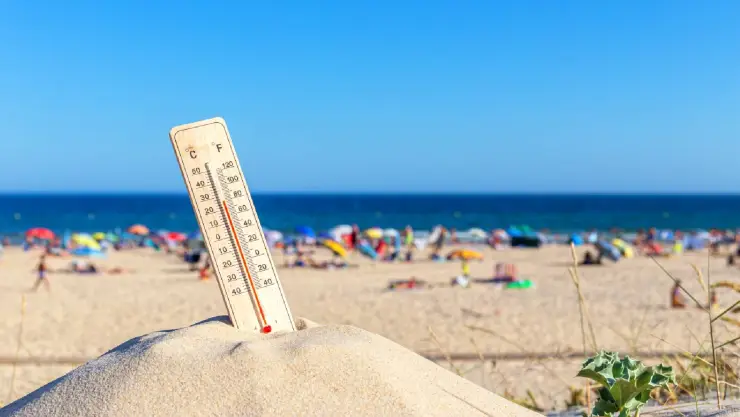 Un termómetro que indica temperaturas sofocantes y la playa de fondo
