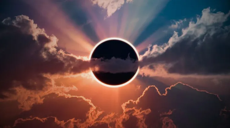 Un eclipse solar total escondido detrás de las nubes. Los rayos del sol se asoman a través de los huecos de las nubes.