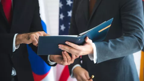 Dos personas revisan una agenda con dos banderas detrás.