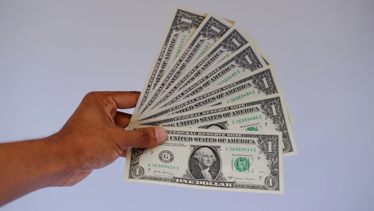 Una mano sostiene varios billetes de un dólar.