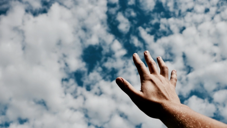 Hombre con mano extendida al cielo con nubes.