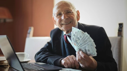 Adulto mayor con mucho dinero en sus manos sentado en su escritorio