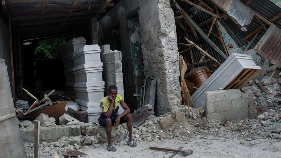 Hombre sentado frente a escombros de una funeraria luego de terremoto en Haití