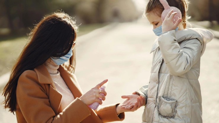 Una madre poniéndole gel desinfectante a su hija con un cubrebocas