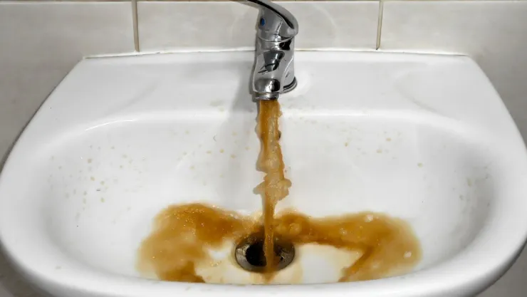 Agua sucia color tierra saliendo del lavamanos de un baño