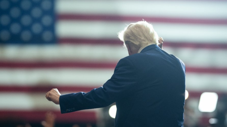 Donald Trump de espaldas frente a una bandera de Estados Unidos durante un evento público en su regreso a la Casa Blanca
