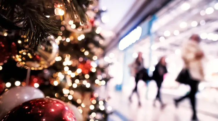 unos compradores caminan y un árbol navideño decora