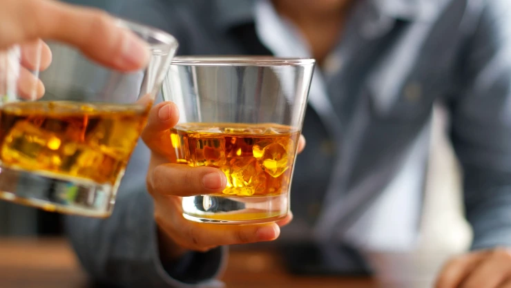 Close-up two men clinking glasses of whiskey drink alcohol beverage together at counter in the pub