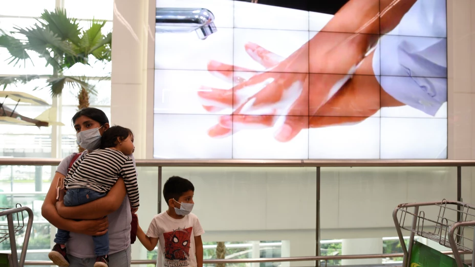 Una mujer y su hijo usan mascarillas cerca de una pantalla que muestra los pasos para lavarse las manos, como parte de las medidas de seguridad debido al brote del coronavirus (COVID-19), en el Aeropuerto Internacional José Joaquín de Olmedo en Guayaquil
