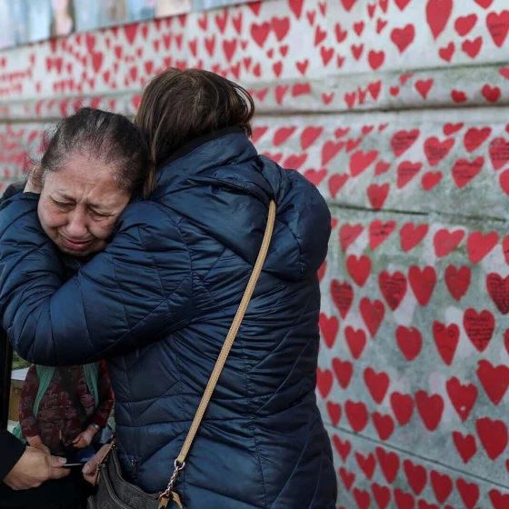 reino_unido_dia_de_reflexion_conmemorar_cinco_anos_pandemia_covid_19_memorial_personas_abrazadas_muro_corazones_rojos