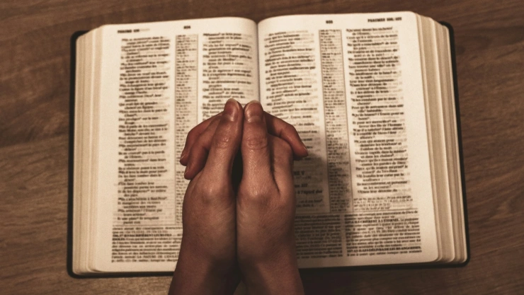 Manos orando sobre biblia abierta.