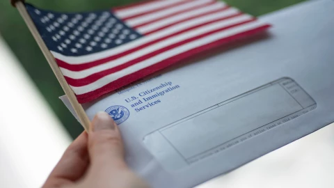 Un sobre del USCIS junto a una bandera estadounidense.