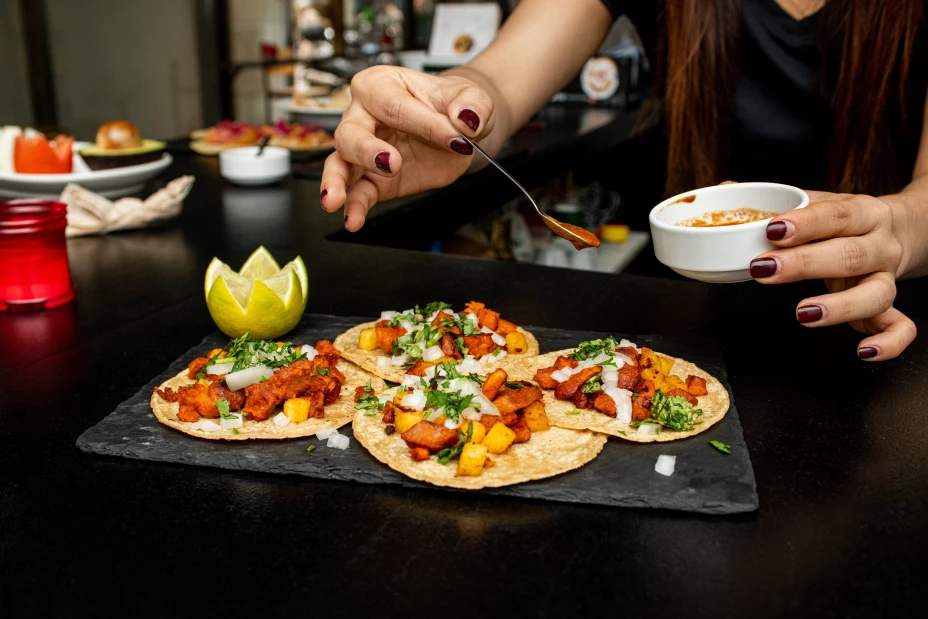 Hand salseado tacos al pastor on a slate plate on the counter of