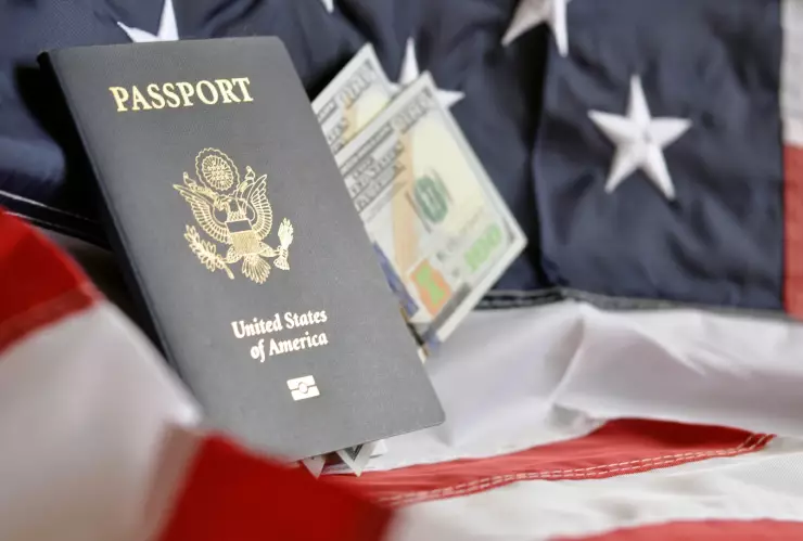 Un pasaporte estadounidense sobre una bandera y billetes de 100 dólares.