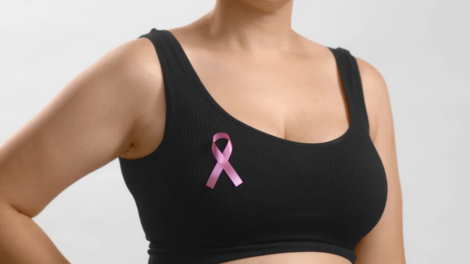 Caucasian unrecognizable woman in a black seamless bra with a pink ribbon for breast cancer. Studio anonymous photo image medium shot on white background.