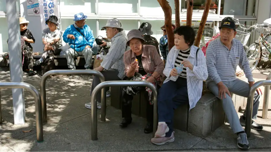Personas mayores descansan a la sombra de un árbol en Tokio.