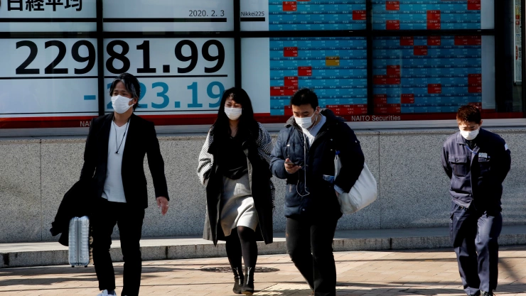 People wearing surgical masks walk past a screen showing Nikkei index outside a brokerage in Tokyo