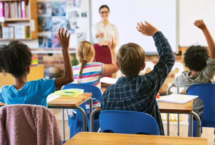 Niños sentados en un aula alzan la mano ante su profesora