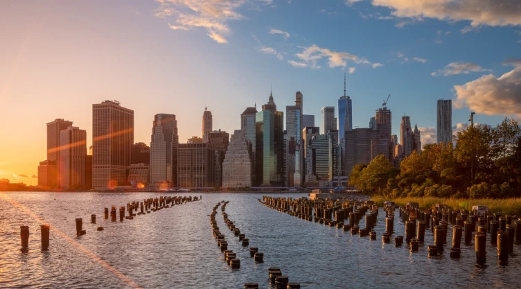 Vista alejada de la ciudad de Nueva York, con el sol cayendo, el río en escena y los edificios gigantes de fondo.