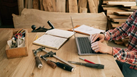 Hombre trabajando frente a la computadora con herramientas de carpintería.