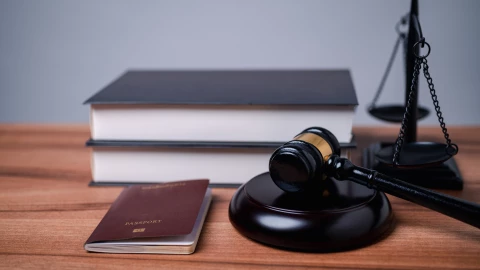 Un pasaporte sobre una mesa, al lado de unos libros y un mazo.